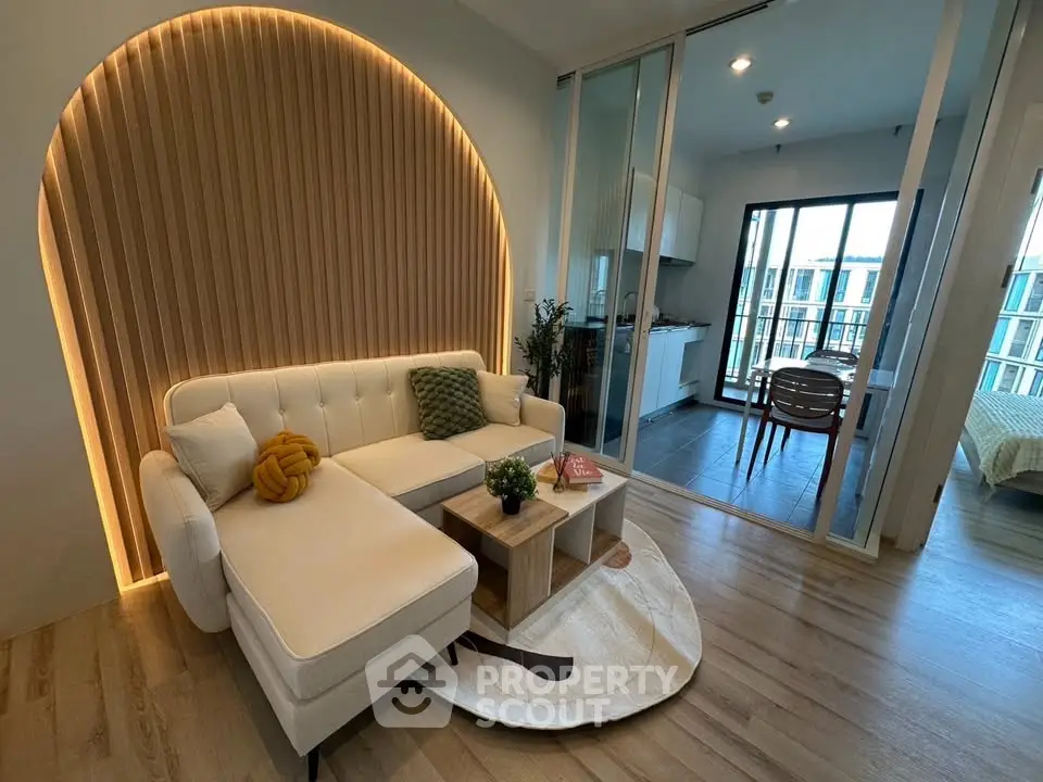 Modern living room with stylish lighting and open layout leading to kitchen and balcony view.