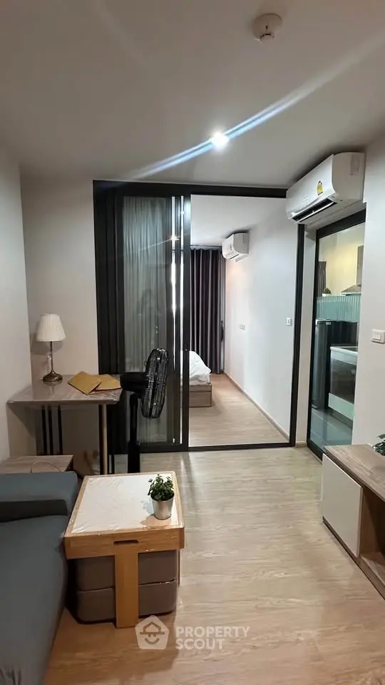 Modern living room with sliding glass doors leading to a cozy bedroom, featuring sleek furniture and wooden flooring.