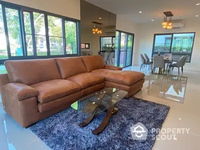 Spacious living room with glossy tiled floors, large leather sectional sofa, and an open-plan layout leading to a modern dining area with abundant natural light.