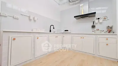 Modern kitchen with sleek white cabinets and wooden flooring, featuring a stylish black faucet and stainless steel range hood.