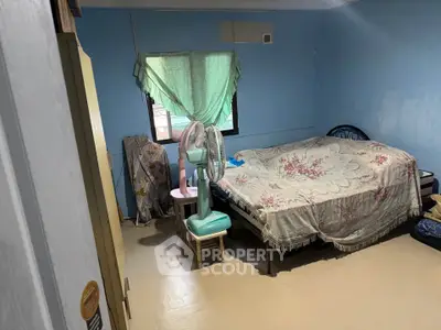 Cozy bedroom with blue walls, window with green curtains, and a fan beside the bed.