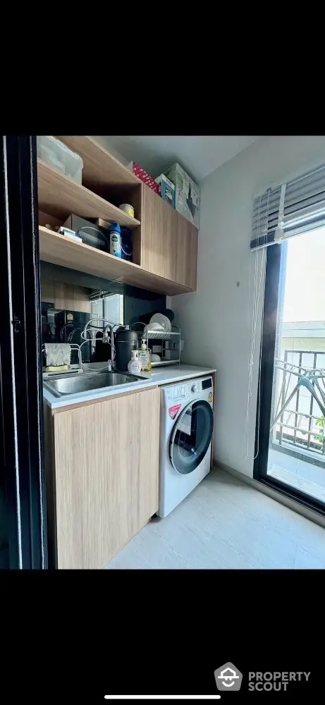 Modern kitchen with washing machine and wooden cabinets, featuring a large window for natural light.