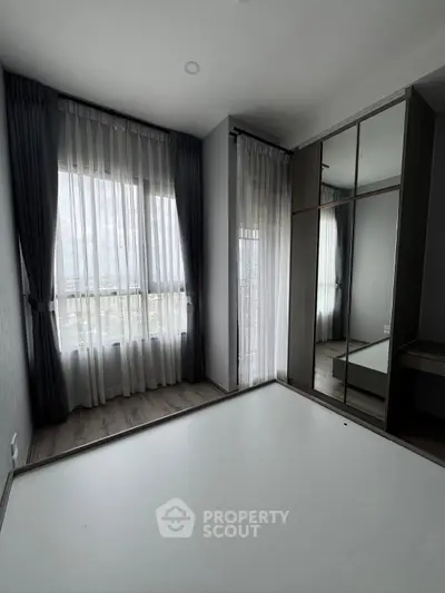 Spacious bedroom with large windows and mirrored wardrobe in modern apartment.