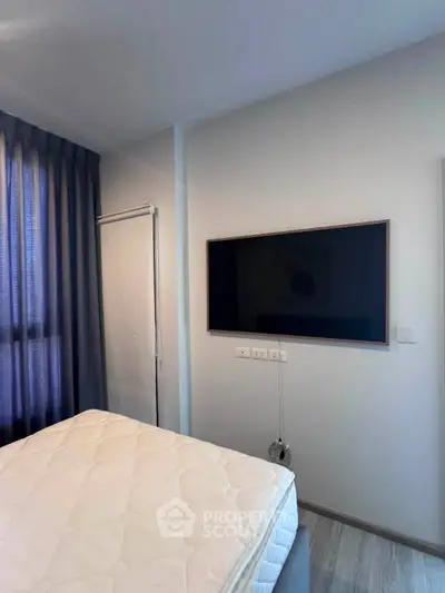 Modern bedroom with wall-mounted TV and cozy mattress, featuring sleek curtains and minimalist design.