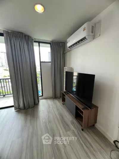 Modern living room with balcony view, featuring sleek TV setup and air conditioning.