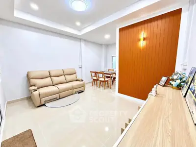 Modern living room with beige sofa and dining area, featuring sleek design and warm lighting.