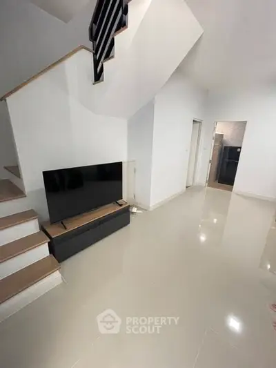 Modern living room with sleek staircase and mounted TV, open layout design.