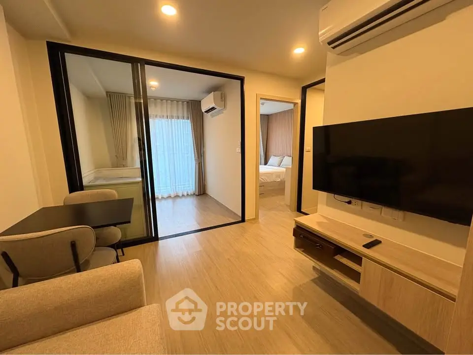 Modern living room with open layout and view into bedroom, featuring sleek furniture and wall-mounted TV.