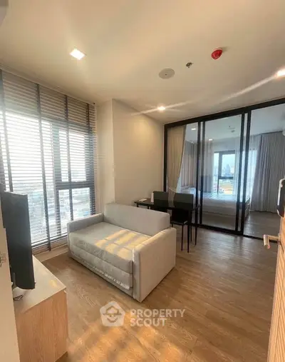 Modern living room with large windows and sliding glass doors, featuring a cozy sofa and wooden flooring.