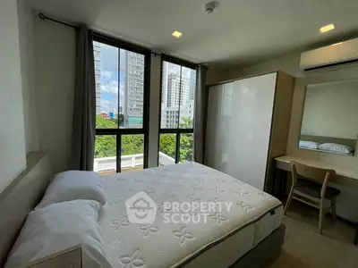 Modern bedroom with large windows and city view, featuring a comfortable bed and sleek furniture.
