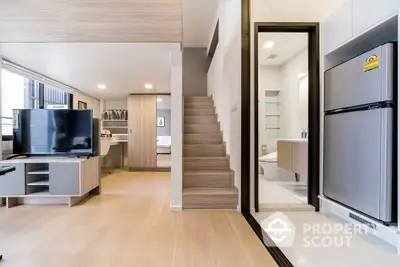 Modern open-plan living space with sleek wooden flooring, featuring a well-equipped kitchen, spacious living area, and an elegant staircase leading to the upper level.