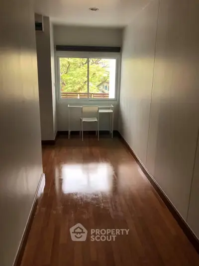 Bright study room with wooden flooring and large window offering lush green views.