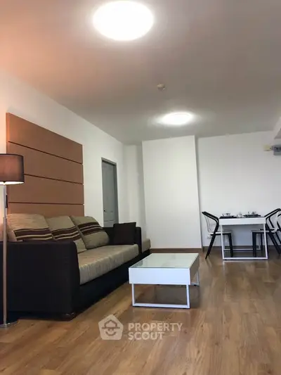 Modern living room with cozy sofa and dining area, featuring sleek wooden flooring and contemporary lighting.