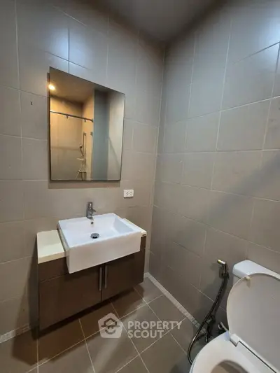 Modern bathroom with sleek sink and mirror, featuring neutral tile design and contemporary fixtures.