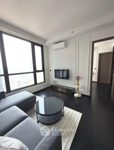 Modern living room with large windows and sleek furniture in a high-rise apartment.
