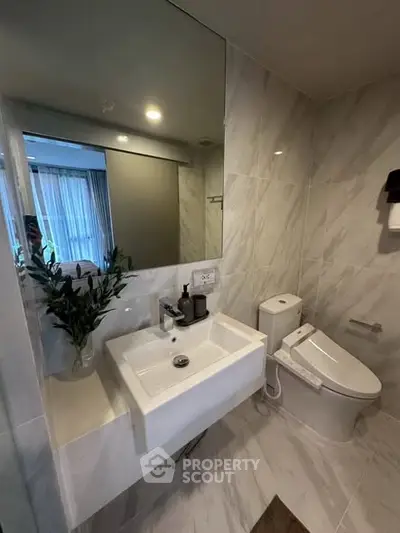 Modern bathroom with sleek fixtures and elegant marble tiles, featuring a stylish sink and toilet.