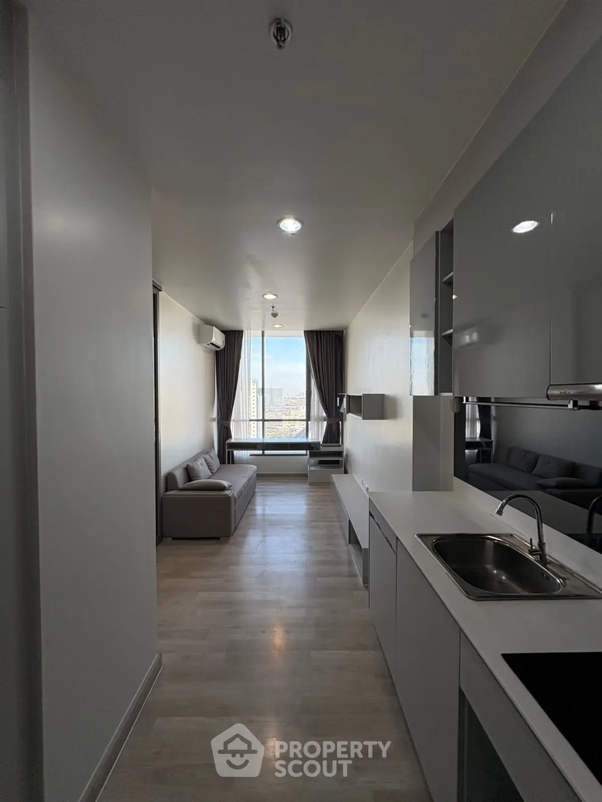 Modern apartment interior with sleek kitchen and cozy living area, featuring large windows with city view.