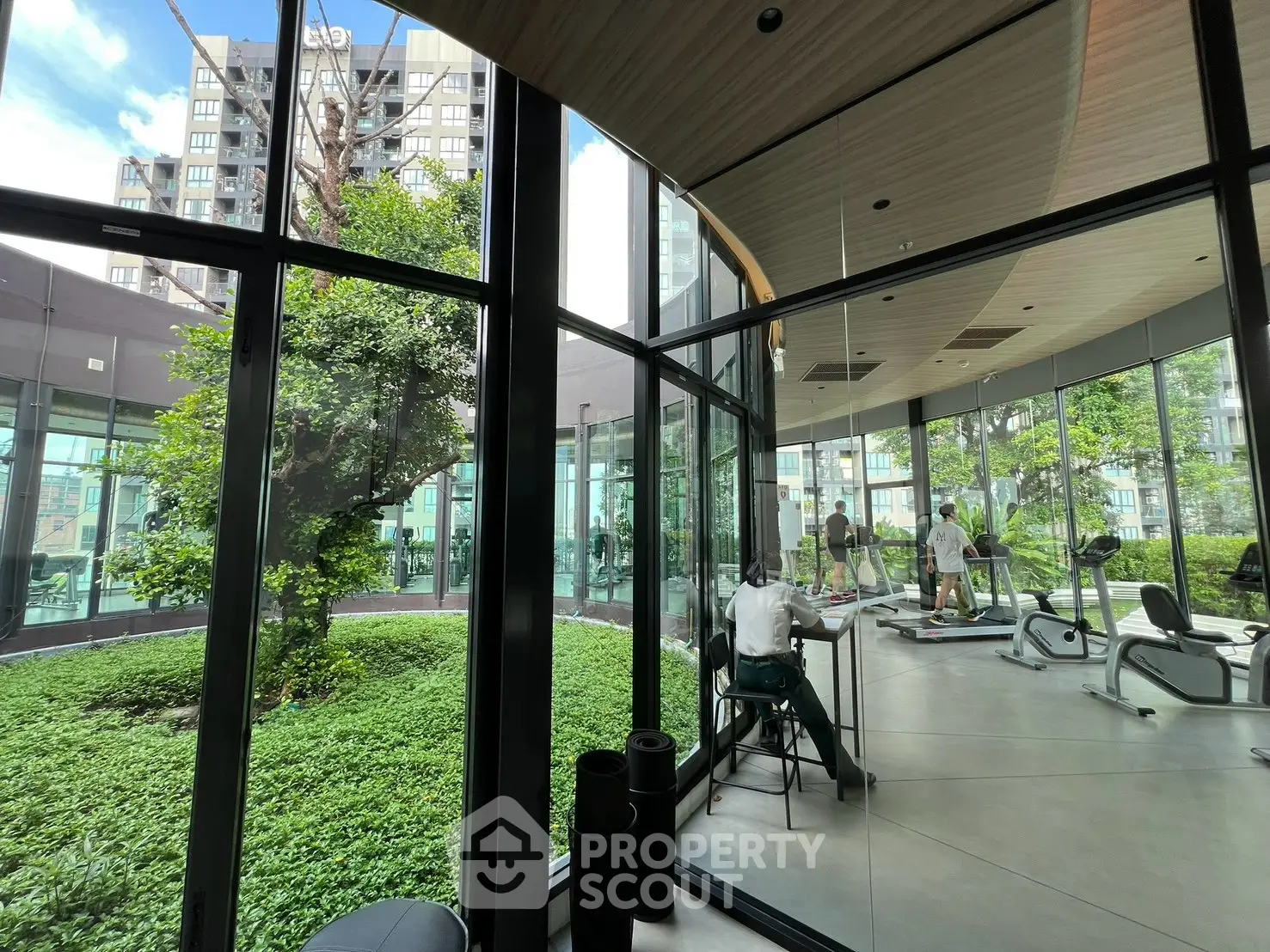 Modern gym with floor-to-ceiling windows overlooking lush garden in luxury residential building.