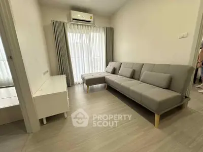 Modern living room with sleek gray sofa and natural light from large window, perfect for relaxation.
