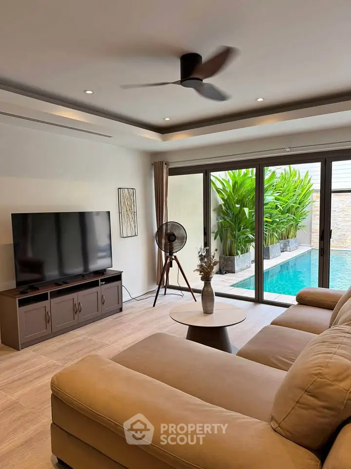 Luxurious living room with pool view, modern decor, and large TV, perfect for relaxation and entertainment.