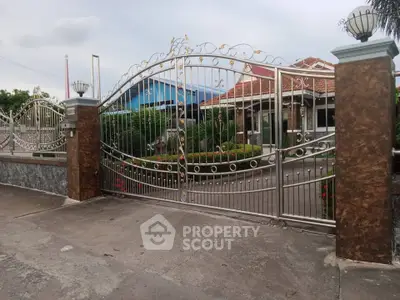 Elegant gated entrance to a charming suburban home with lush garden and paved driveway.