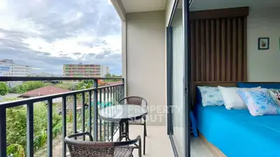 Spacious balcony with outdoor seating connected to a cozy bedroom with vibrant blue bedding, offering a serene urban view and ample natural light.