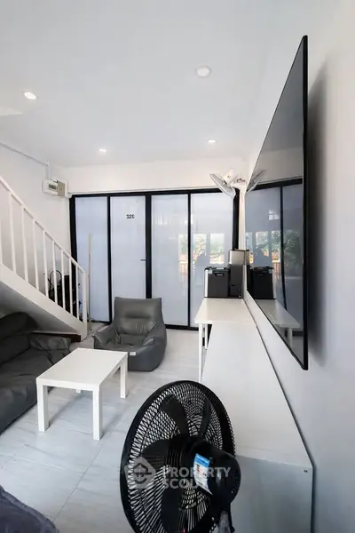 Modern living room with sleek design, featuring a large TV, comfortable seating, and natural light.