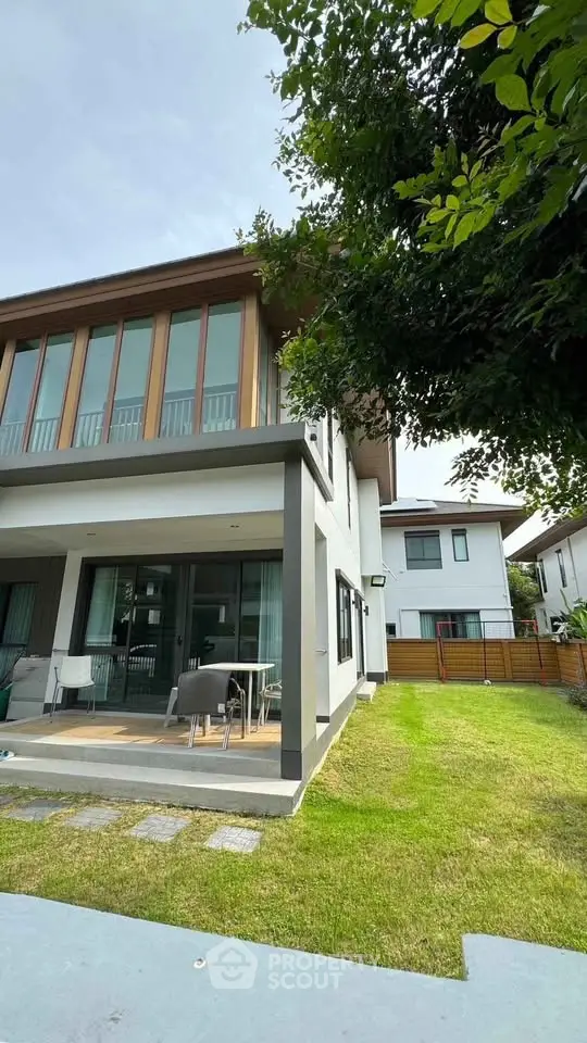 Modern two-story house with large windows and lush green lawn in a serene neighborhood.
