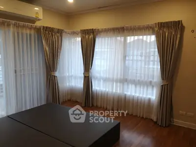 Spacious bedroom with elegant curtains and wooden flooring, perfect for cozy living.