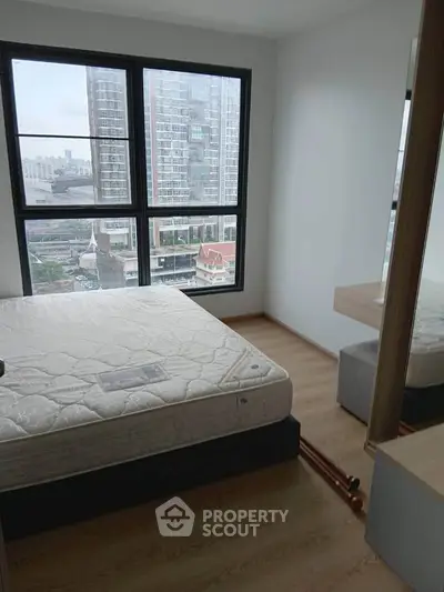Modern bedroom with large window offering city view, featuring a comfortable bed and wooden flooring.
