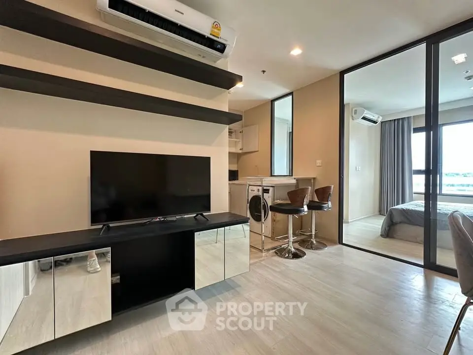 Modern apartment interior with open living room and kitchen, featuring sleek furniture and natural light.