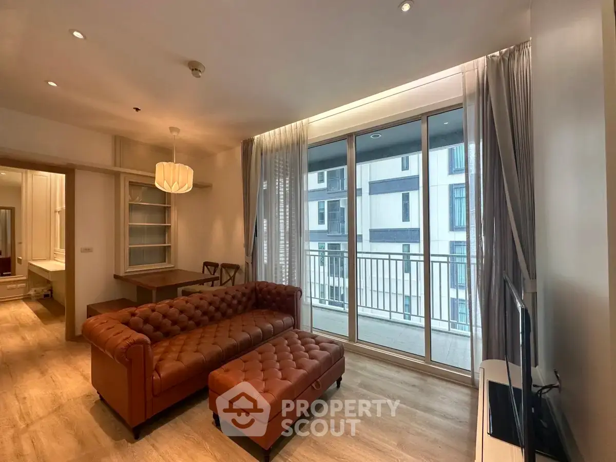 Spacious living room with elegant leather sofa and large windows leading to a balcony in modern apartment.