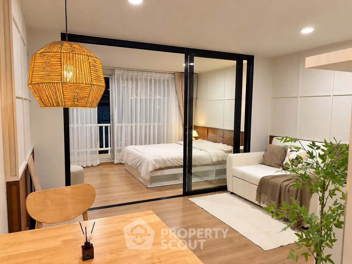 Modern open-plan living room with cozy bedroom view, featuring stylish decor and warm lighting.