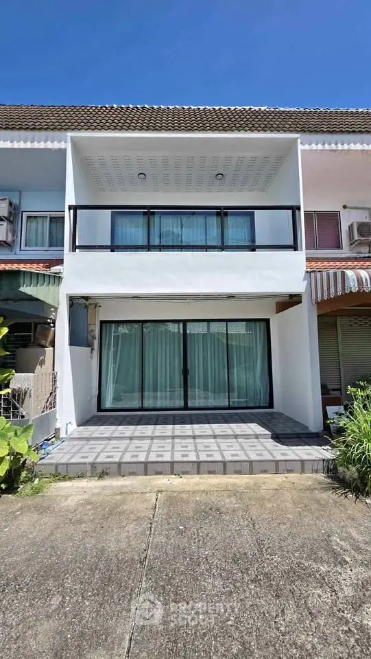 Modern townhouse exterior with balcony and large glass doors under clear blue sky.