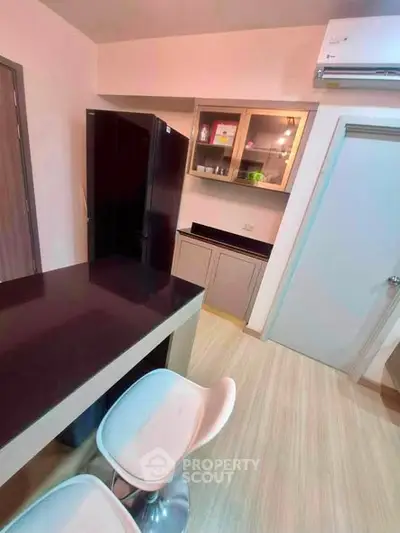 Modern kitchen with sleek black fridge and stylish bar stools in a cozy apartment.