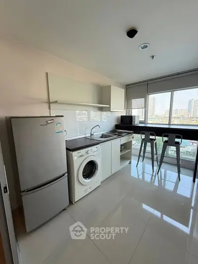 Modern kitchen with sleek appliances and city view, featuring a washing machine and breakfast bar.
