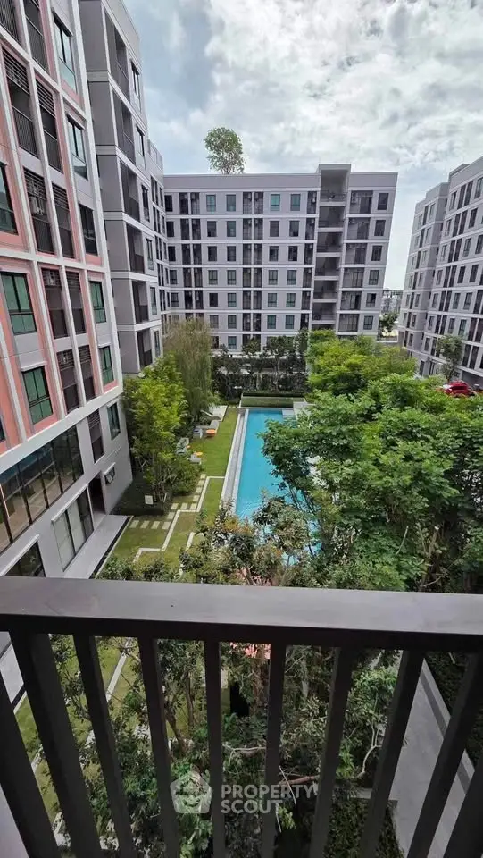 Modern apartment complex with pool view from balcony, lush greenery and stylish architecture.