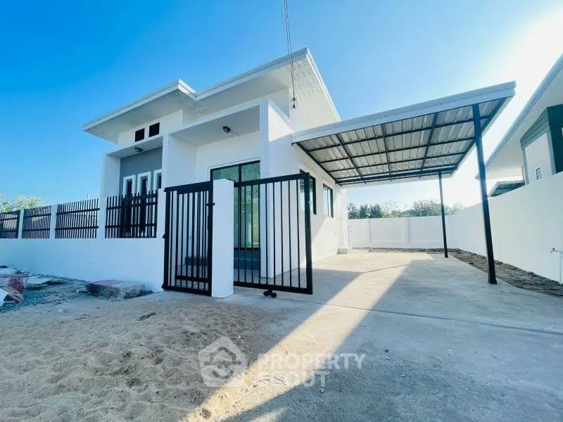 Modern single-story house with spacious driveway and sleek metal gate, perfect for contemporary living.