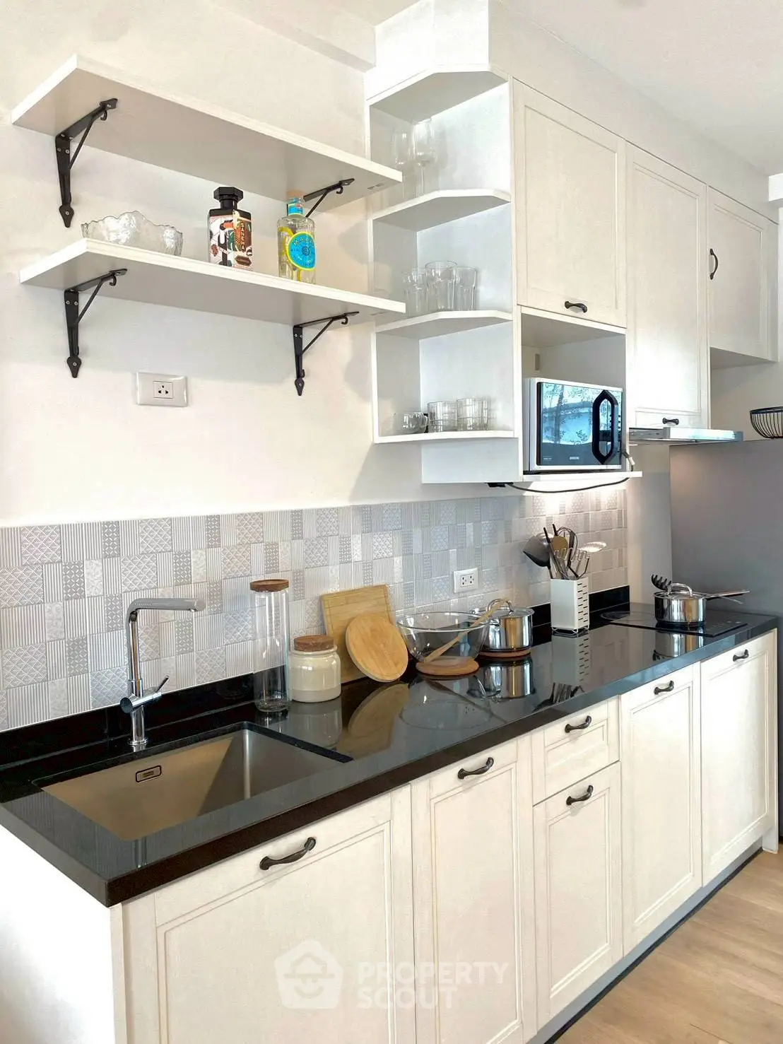 Modern kitchen with sleek black countertops and open shelving, featuring a microwave and stylish backsplash.