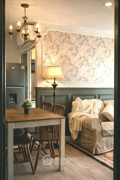 Cozy living room with elegant chandelier and floral wallpaper, featuring a comfy sofa and dining area.