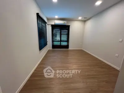 Spacious empty room with wooden flooring and large window, perfect for customization.