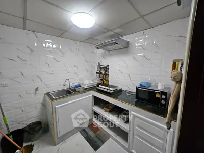 Modern kitchen with sleek white cabinets and black countertop, featuring a microwave and sink.