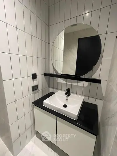 Modern bathroom with sleek sink and round mirror, featuring contemporary tile design.