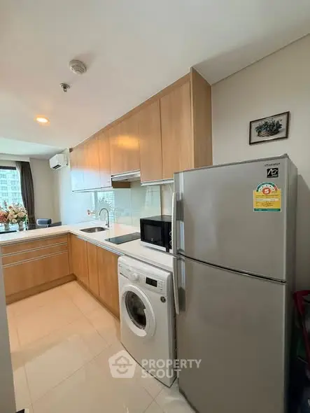 Modern kitchen with wooden cabinets, fridge, and washing machine in a cozy apartment.