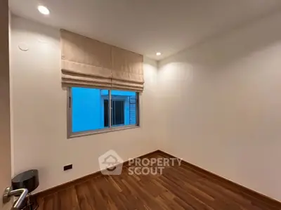 Spacious empty room with wooden flooring and large window, perfect for customization.
