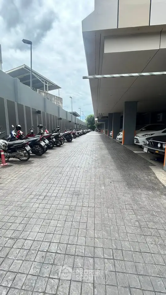 Spacious parking area with motorcycles and cars in a modern building complex.