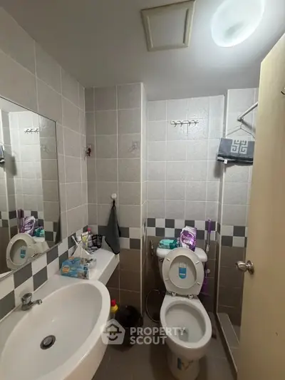 Compact bathroom with modern fixtures and tiled walls, featuring a sink, toilet, and mirror.
