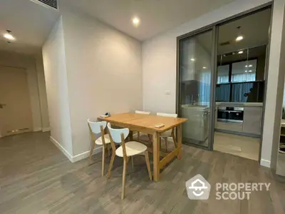 Modern dining area with wooden table and chairs next to a sleek kitchen with glass partition.