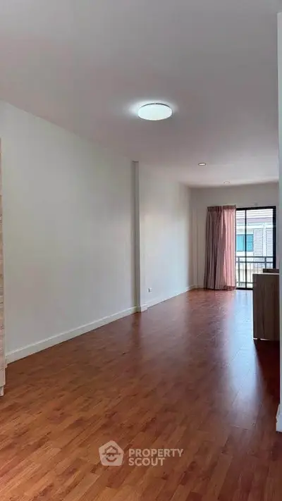 Spacious living room with wooden flooring and balcony access in modern apartment.