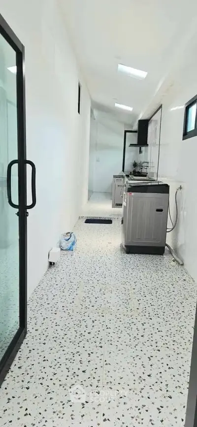 Modern kitchen with sleek appliances and terrazzo flooring in a bright, narrow layout.